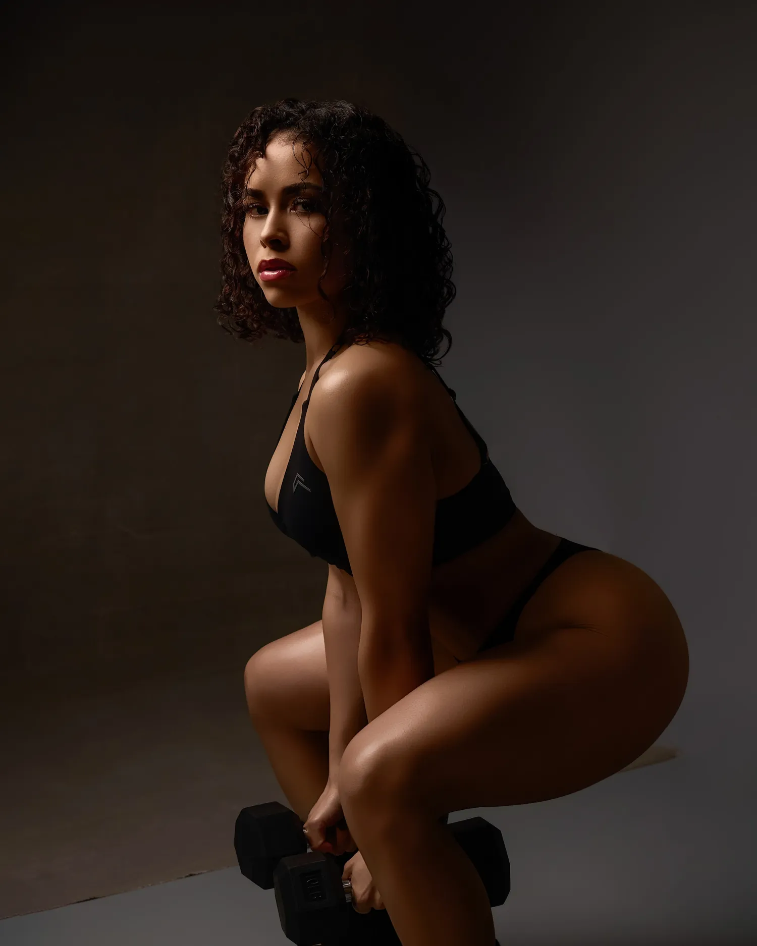 Alexa holding dumbbells in a deep squat, studio portrait