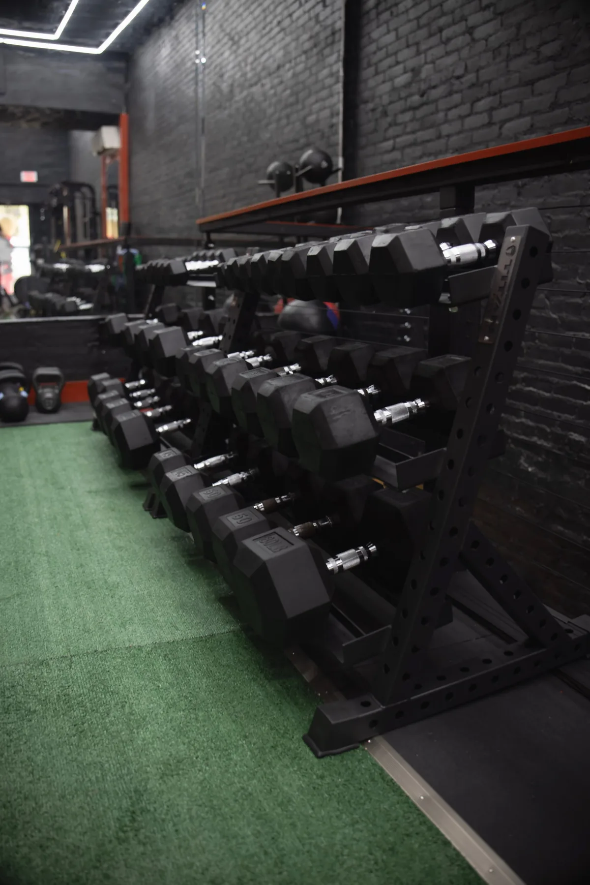 Rows of dumbbells on the turf at Body Built By You, black brick walls and red trim